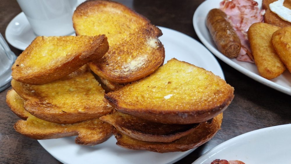 Thick slices of golden fried bread on a plate, breakfasts behind